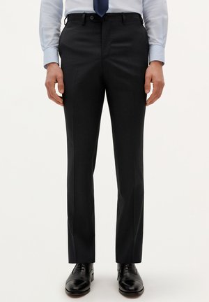 Pantalones oscuros grises a medida con una textura suave, corte recto, bolsillos laterales y presillas para cinturón, combinados con zapatos de vestir negros.