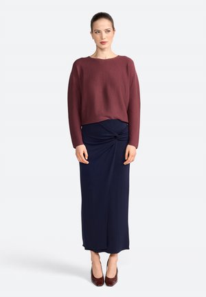 Maroon knit sweater with a round neckline, paired with a navy blue, knee-length skirt featuring a twisted detail at the waist. Brown heels.