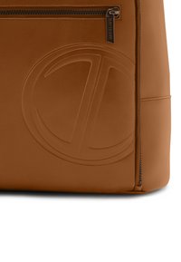 Brown leather bag featuring a prominent embossed logo, smooth texture, zippered closure, and minimalistic design with angular shapes.