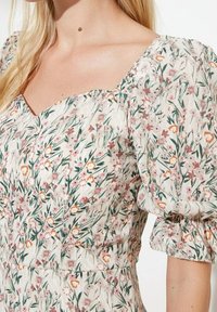 Robe à motif floral avec décolleté carré, manches courtes bouffantes et corps ajusté en tissu léger et doux dans des couleurs pastel.