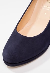 Chaussure plate en daim bleu marine avec bout arrondi et intérieur en cuir beige sur fond blanc.