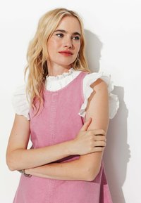Robe sans manches rose avec une finition texturée, dotée de manches blanches à volants et d'un col monté. Coutures minimales, silhouette simple.