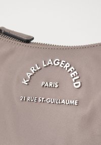 Grå nylonväska med silverpräglad logotext: "KARL LAGERFELD PARIS" och adress "21 RUE ST-GUILLAUME." Dragkedjestängning.