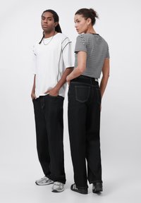 Svarte vide jeans kombinert med en hvit oversized T-skjorte og en svart-hvit stripete tettsittende topp. Begge har på seg casual sneakers.