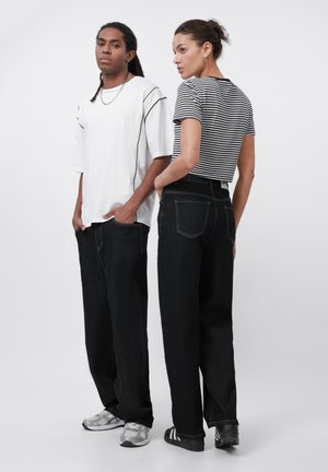 Black wide-leg jeans paired with a white oversized T-shirt and a black-and-white striped fitted top. Both wear casual sneakers.