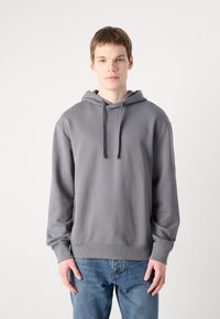 Grijze hoodie met een trekkoordkap en ribbelmanchetten, met een subtiele logo op de borst. Gecombineerd met blauwe spijkerbroek.