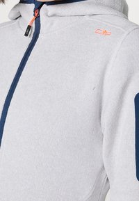 Gray zip-up hoodie made of textured fabric with a navy blue zipper and arm accents. Features a hood and an orange logo on the shoulder.