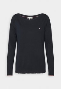 Pull noir à manches longues avec col rond, petit logo rouge, blanc et bleu sur la poitrine gauche, et poignets côtelés avec bordure rouge et blanche.