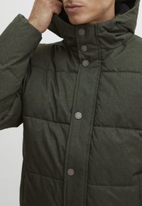 Green puffer jacket made of textured, quilted fabric. Features a high collar and silver-tone snap buttons along the front.