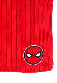 Rode gebreide beanie met verticale ribbels en een geborduurd rond Spider-Man-logo met grote witte ogen en webpatroon. Zachte textuur.