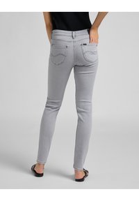 Jeans gris ajustados fabricados con denim elástico, que presentan una cintura de altura media, bolsillos traseros y detalles de costura sutil a lo largo de las costuras.