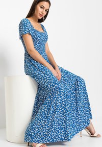 Abito lungo blu con motivo floreale bianco, corpino aderente, maniche corte e orlo svasato. Tessuto morbido, design fino alla caviglia.