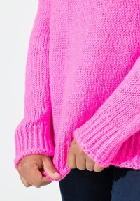 Sweater tricoté rose vif avec des poignets côtelés, un tissu texturé et une coupe ample, tenu par l'ourlet.