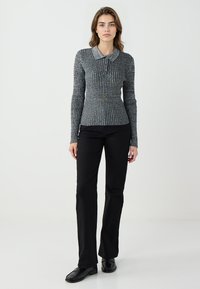 Top a maniche lunghe con bottoni, a righe blu scuro e beige, con scollo con colletto; abbinato a pantaloni neri svasati e mocassini neri.