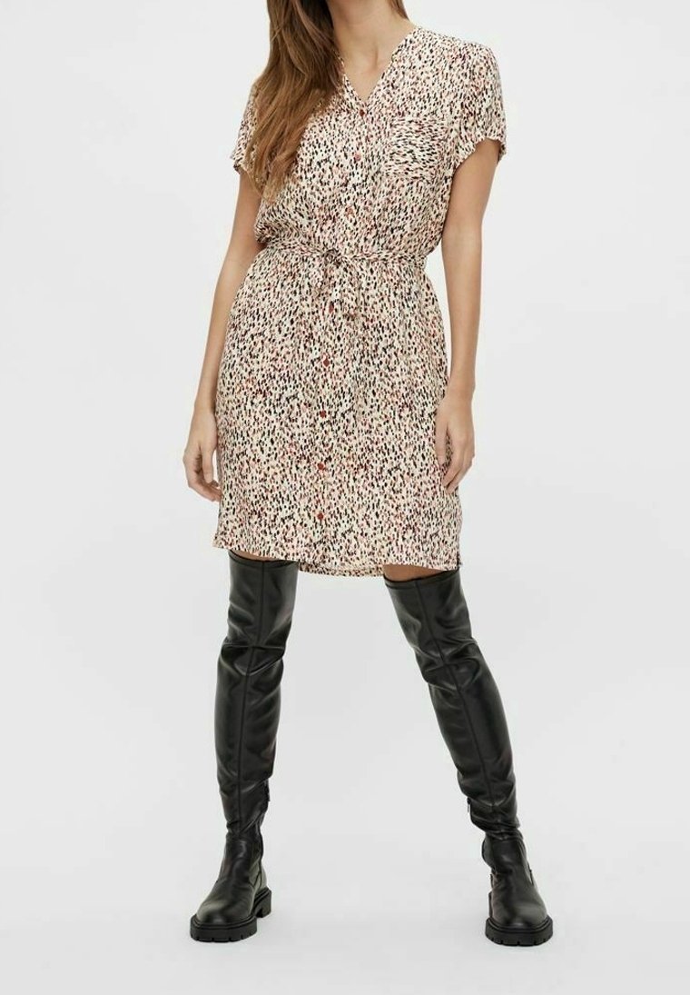 Robe courte à manches courtes, longueur genou, en beige clair avec des taches noires et rouges, dotée d'une taille cintrée et d'un devant boutonné. Portée avec des bottes noires montant jusqu'aux genoux.