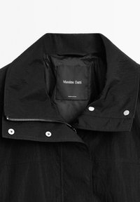 Svart Massimo Dutti-jacka med krage, silverfärgade tryckknappar och delvis synlig dragkedja, med varumärkets etikett inuti.