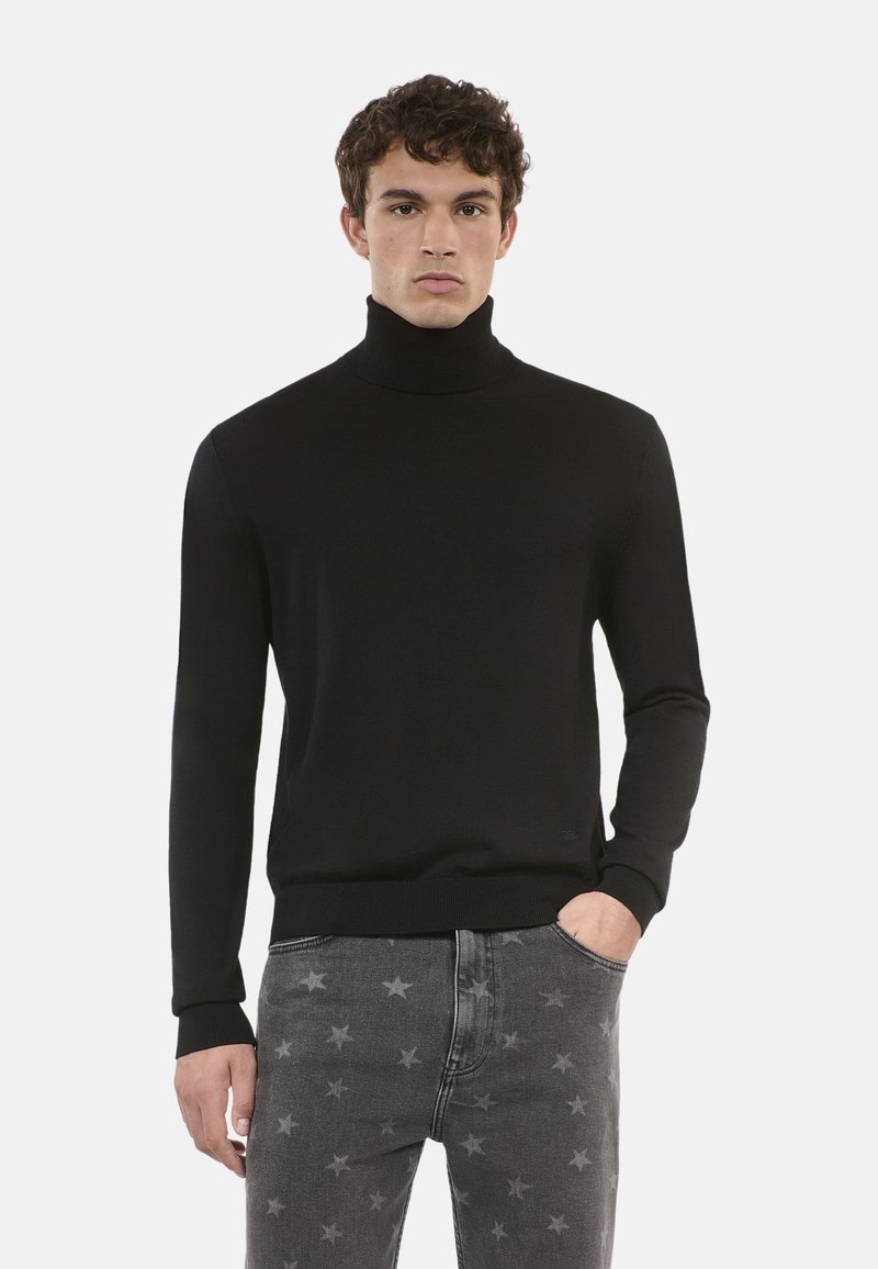 Maglione a collo alto nero in un tessuto morbido, dal design aderente con maniche lunghe, abbinato a jeans grigi con motivo a stelle.