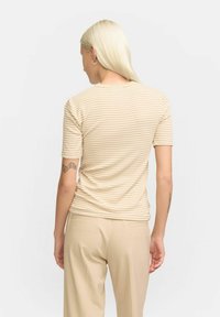 Beige stribet t-shirt med korte ærmer, rund halsudskæring og blødt stof. Båret med lyse bukser, der viser et afslappet fit.