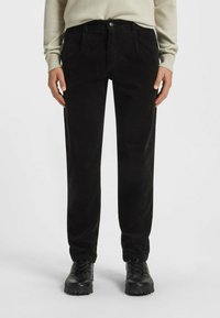 Czarne spodnie w kordówkę, o prostym kroju, z bocznymi kieszeniami i zapięciem na guzik, zestawione z czarnymi wiązanymi botkami za kostkę.