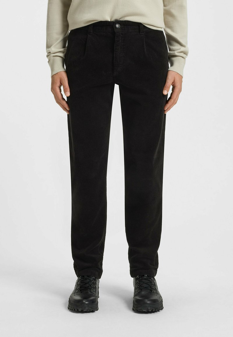 Czarne spodnie w kordówkę, o prostym kroju, z bocznymi kieszeniami i zapięciem na guzik, zestawione z czarnymi wiązanymi botkami za kostkę.