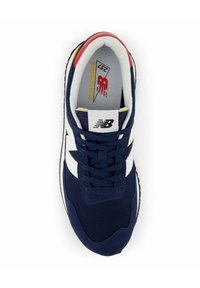 Zapatilla de malla azul marino con acentos blancos, punta redonda y suela negra. Presenta el logo de New Balance y detalles multicolores en el talón.