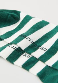 Chaussettes rayées vertes et blanches en matériau doux avec un design à revers. Présente un petit logo noir sur le corps des chaussettes.