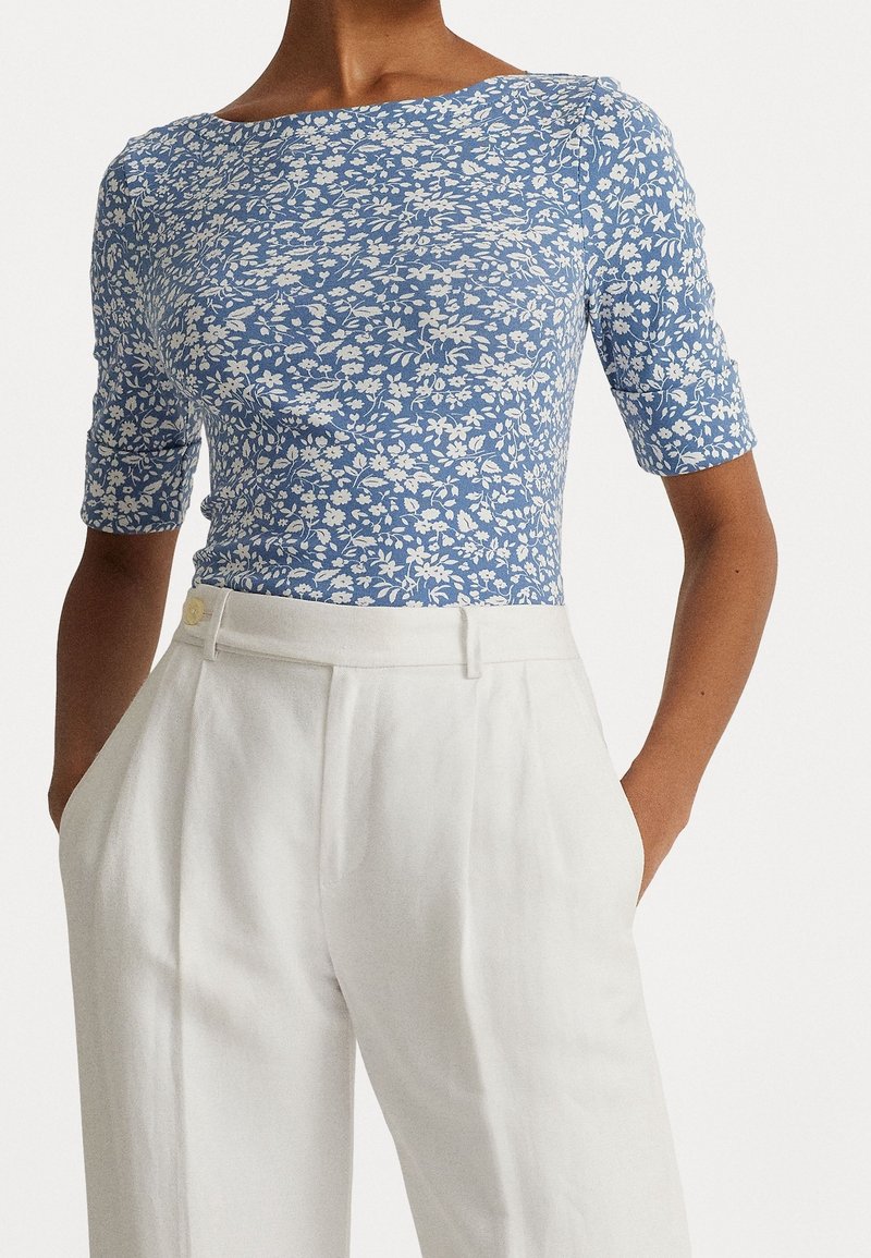 Blå blommönstrad topp med korta ärmar och båthalsringning, tillsammans med högmidjade vita byxor med ficka fram och knapprad.