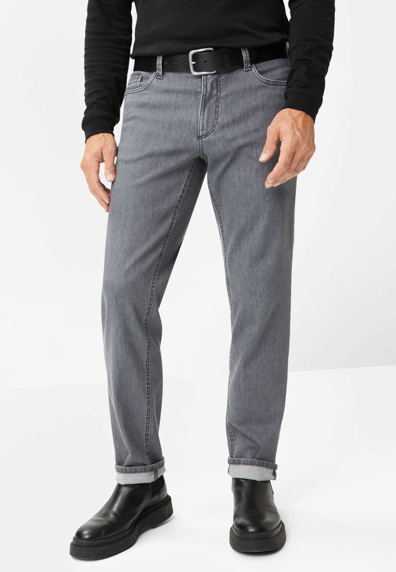 Graue Jeans aus Denim mit geradem Schnitt, umgeschlagenen Säumen, subtilen Nähten, Fronttaschen und kombiniert mit schwarzen Lederstiefeln.