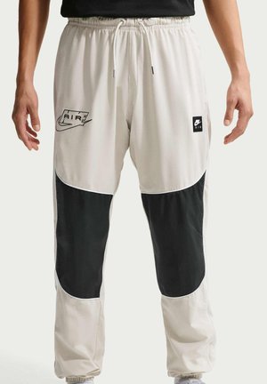 Beige og sorte Nike træningsbukser til mænd med elastisk talje, snøre og Nike Air-logoer på forreste lårpaneler.