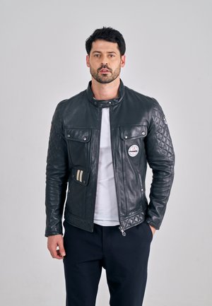 Zwarte leren motorjack met doorgestikte textuur, drukknoopsluiting en twee borstzakken. Voorzien van een rond logopatch en strepen op de zak.