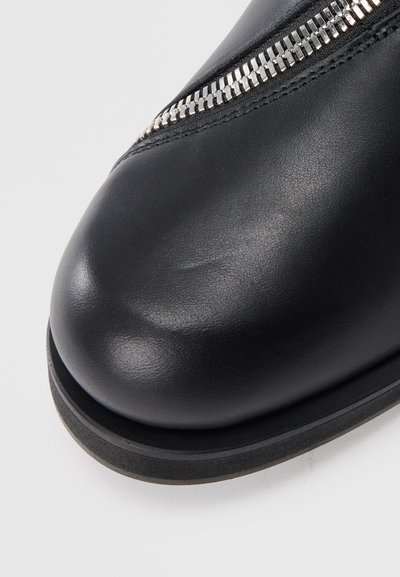 Black leather ankle boot with a rounded toe, featuring a silver zipper detail on the side and a flat rubber sole. Smooth texture.