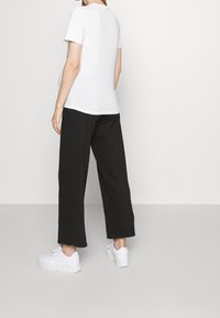 Valkoinen lyhythihainen t-paita yhdistettynä väljät mustat housut ja valkoiset lenkkarit, esittelee rentoa ja mukavaa tyyliä.