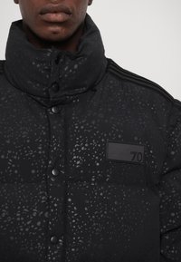 Black puffer jacket with a high collar, featuring a textured surface and shiny accents. Includes a rectangular label with the number 70.