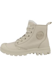 Bottes de cheville en cuir beige clair avec une semelle texturée, un col rembourré et un patch logo bien visible sur le côté. Caractéristiques : bout rond et design à lacets.