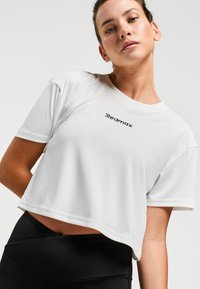 T-shirt de sport blanc cropped en tissu lisse, avec un col rond et le logo "Redmax" en noir à l'avant.