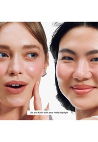 Deux femmes à la peau éclatante et mise en valeur ; l'une touche sa joue tandis que toutes deux sourient doucement sur un fond blanc.