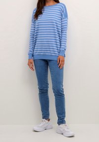 Pull surdimensionné rayé bleu et blanc à manches longues, associé à un jean bleu ajusté et des baskets blanches. Tissu doux, coupe décontractée.