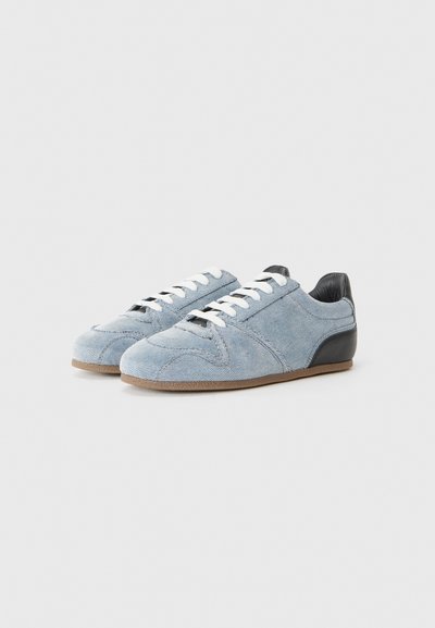 Blue suede sneakers feature a low profile, white laces, and a black leather heel accent. The outsole is light brown with textured detail.