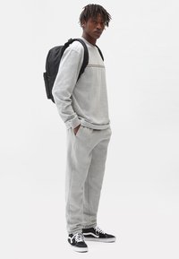 Gray sweatshirt with a round neckline and horizontal stripes, paired with matching sweatpants; black backpack and sneakers complete the look.