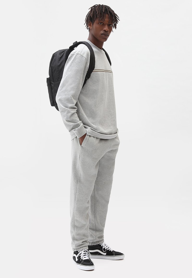 Grijze sweatshirt met een ronde hals en horizontale strepen, gecombineerd met bijpassende joggingsbroek; een zwarte rugzak en sneakers maken de look compleet.