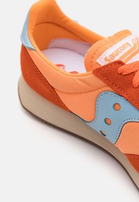 Pomarańczowo-brzoskwiniowy sneaker z niebieskimi akcentami, wykonany z zamszu i materiałów syntetycznych, z okrągłym noskiem, teksturowanymi sznurowadłami oraz oznaczeniami na języku.