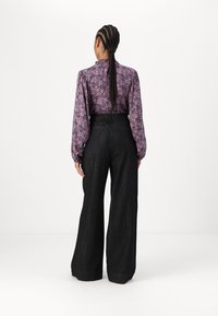 Floral patterned purple blouse with puffed sleeves paired with high-waisted dark denim wide-leg pants. Smooth texture, minimal hardware.