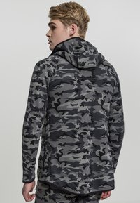 Sudadera con capucha en un patrón de camuflaje negro y gris, que presenta mangas largas, diseño ajustado y una suave tela con textura.