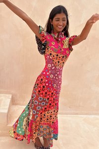 Maxi-jurk met een levendig patchwork van bloem- en geometrische patronen in rood, roze en groen, met gerimpelde mouwen en een getailleerde silhoët.