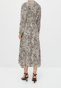 Robe midi avec une base beige à motifs léopard noirs, manches longues et taille cintrée. Associée à des talons noirs à lanières.