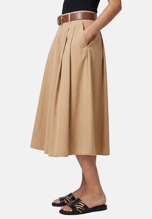 Falda midi plisada beige con bolsillos, cinturón marrón, combinada con sandalias planas tipo slide con estampado animal en negro y marrón claro.