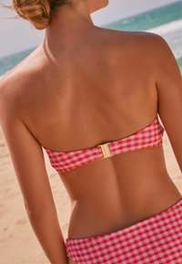 Rood en wit geruit bikini-top met een gouden sluiting aan de achterkant. Glad textuur, strapless ontwerp, gecombineerd met bijpassende geruite onderkant.