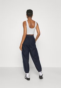 Person standing facing away wearing a gray sleeveless crop top, dark blue loose pants, white Adidas socks, and black Adidas sneakers.