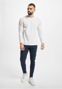 Hvit langermet skjorte, mørkeblå smale jeans og hvite joggesko. Minimalistisk design, jevn tekstur og tettsittende form.