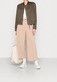 Giubbotto bomber verde oliva, pantaloni beige a gamba larga, stivaletti bianchi alla caviglia e borsa a tracolla beige. Design semplice, texture morbida e colori neutri.